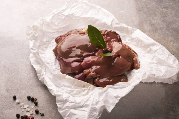 Raw chicken livers on a paper on stony countertop. Poultry, giblets, horizontal view.