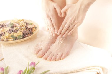 Evdeki genç bir kadın ayak soyma ve el kalp hareketi yapıyor. Vücut bakımı, pedikür, lalelerle süslenmiş rahat bir yerde ayak masajı. Sağlık ve Gündüz Spa, Güzellik Salonu. Kadınlar Günü.