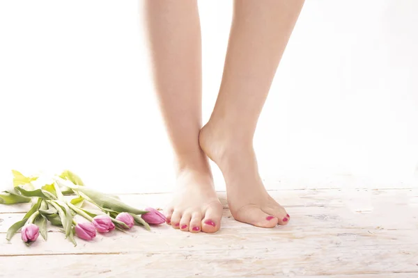 Young, female naked, bare feet with pink painted toenails on wood floor decorated with tulips. Correct foot posture. Feet without flat feet. Podology. Foot care, SPA, salon, pedicure. Women\'s Day