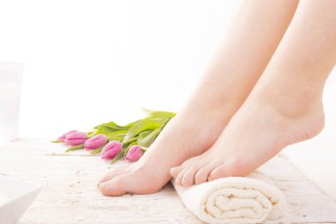 Genç, çıplak, çıplak ayaklı, tahta zeminde doğal çivili, lalelerle süslenmiş. Doğru ayak duruşu. Düz tabansız ayaklar. Podoloji. Ayak bakımı, SPA, kuaför, pedikür. Kadınlar Günü