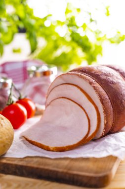 Tavuk tek parça halinde kesilir ve dilimlenir. Kağıt üzerinde dilimlenmiş kümes hayvanları, ahşap bir kesme tahtasında. Tütsülenmiş, domatesli tavuk eti ve taze otlardan oluşan kaba bir kompozisyon..