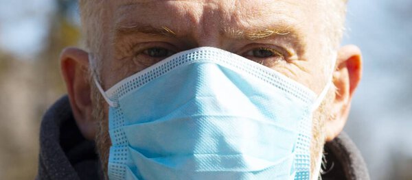 Close-up of a man in a surgical mask standing outdoor. Virus infection protection kit. Rapidly spreading corona pandemic.
