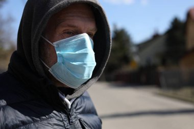 Güneşli bir günde tek kullanımlık cerrahi maske ve kapüşonlu orta yaşlı kızıl saçlı adam dışarıda dikiliyor. Koronavirüs enfeksiyonuna karşı koruma. Çin, Wuhan 'dan hızla yayılan bir virüs salgınıyla savaşıyor.
