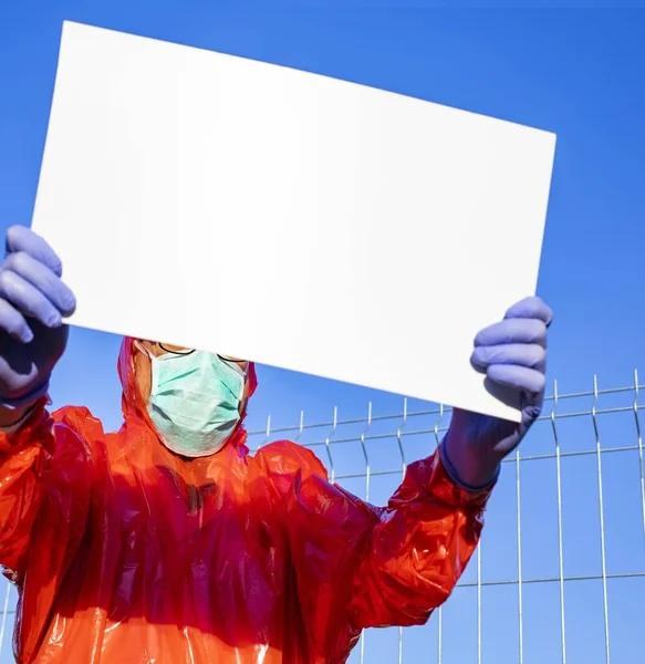 一个身穿防护服的男人 戴着手套 外科口罩 拿着一块空白板 带着版权 在阳光明媚的日子里站在室外 阻止来自中国武汉的Sars病毒大流行 — 图库照片