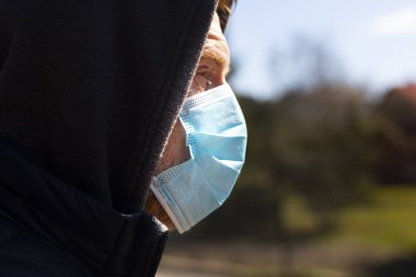 Güneşli bir günde tek kullanımlık maske takmış kızıl saçlı bir adamın yan görüntüsü. Koronavirüs enfeksiyonuna karşı koruma. Çin, Wuhan 'dan hızla yayılan bir virüs salgınıyla savaşıyor.