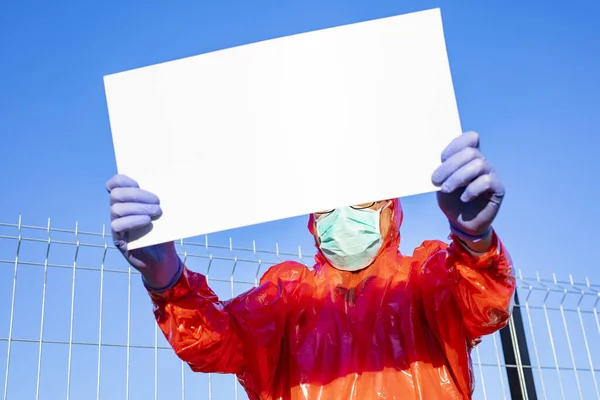 一个身穿防护服的男人 戴着手套 外科口罩 拿着一块空白板 带着版权 在阳光明媚的日子里站在室外 阻止来自中国武汉的Sars病毒大流行 — 图库照片