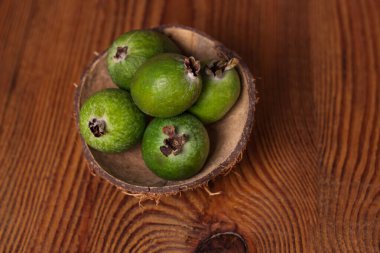 Ahşap bir arka planda hindistan cevizi kabuklu bir gövde içinde yeşil feijoa. Olgun tropikal meyveler, çiğ vegan yiyecekler. C vitamini..