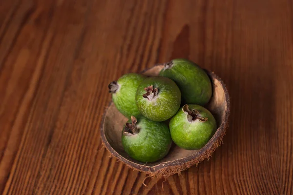 Green feijoa in a coconut shell hulf on a wooden background. Ripe tropical fruits, raw vegan food.Vitamin C. Copy space.