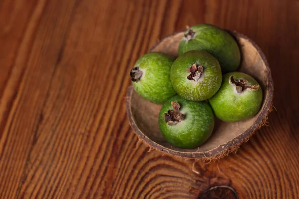 Green feijoa in a coconut shell hulf on a wooden background. Ripe tropical fruits, raw vegan food.Vitamin C. Copy space.