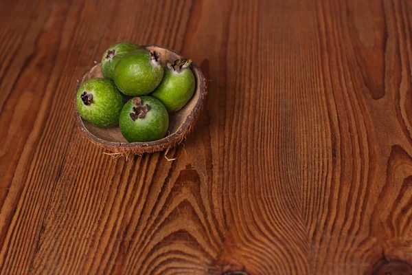 Green feijoa in a coconut shell hulf on a wooden background. Ripe tropical fruits, raw vegan food.Vitamin C. Copy space.