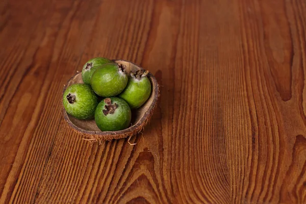 Green feijoa in a coconut shell hulf on a wooden background. Ripe tropical fruits, raw vegan food.Vitamin C. Copy space.