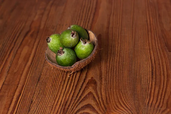 Green feijoa in a coconut shell hulf on a wooden background. Ripe tropical fruits, raw vegan food.Vitamin C. Copy space.