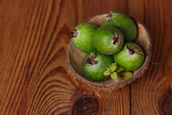 Green feijoa in a coconut shell hulf on a wooden background. Ripe tropical fruits, raw vegan food.Vitamin C. Copy space.