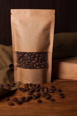 Tahta arka planda şeffaf pencerede kahve çekirdekleri olan boş kahverengi bir kese kağıdı. Çay için modaya uygun ambalaj