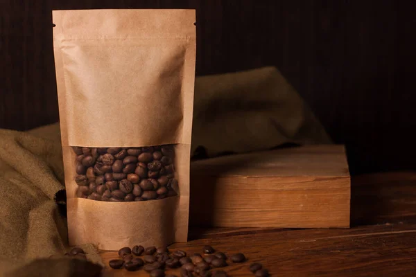 Bolsa de papel kraft marrom em branco com grãos de café em janela transparente no fundo de madeira. Embalagem na moda para chá — Fotografia de Stock