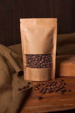 Tahta arka planda şeffaf pencerede kahve çekirdekleri olan boş kahverengi bir kese kağıdı. Çay için modaya uygun ambalaj