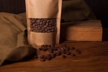 Tahta arka planda şeffaf pencerede kahve çekirdekleri olan boş kahverengi bir kese kağıdı. Çay için modaya uygun ambalaj