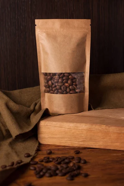 Bolsa de papel kraft marrom em branco com grãos de café em janela transparente no fundo de madeira. Embalagem na moda para chá — Fotografia de Stock