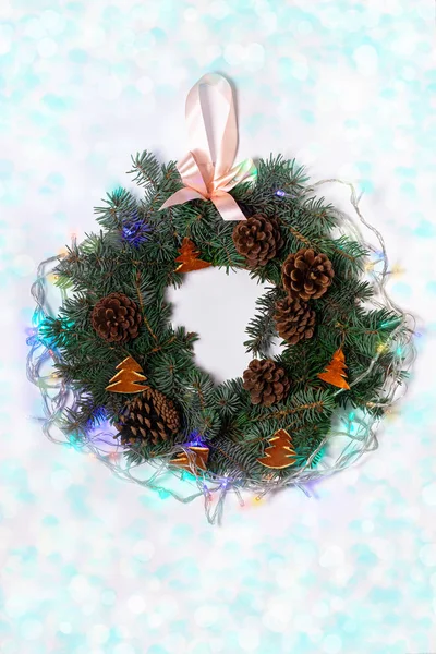 Christmas wreath flatlay. Green spruce decorated with orange zest, lights, pine cones and ribbon on white background.