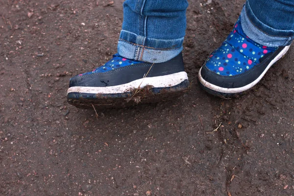 Παιδικές μπότες σε λασπωμένη λακκούβα. Πολύχρωμα χειμερινά υπαίθρια παπούτσια βροχής σε παιδικά πόδια σε δράση. Ένα παιδί που μένει στη λάσπη.. — Φωτογραφία Αρχείου