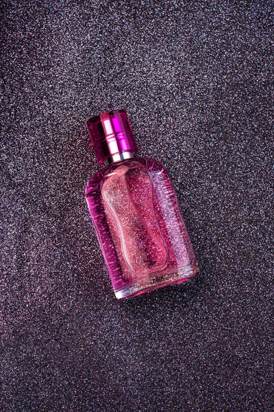 Pink woman perfume bottle on dark shiny black glitterring background, top view. Trendy colors flatlay,beauty blog banner