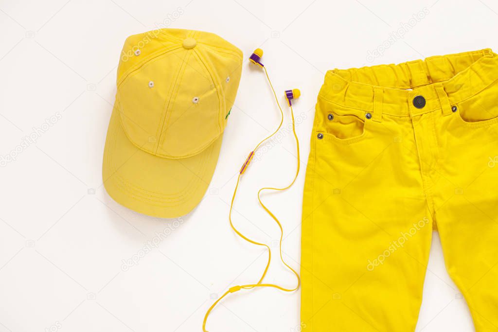 Yellow flatlay jeans, baseball cap and headphones on white background copy space,top view.Spring summer fashion clothing