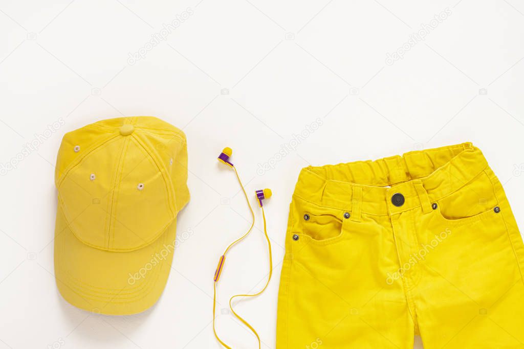 Yellow flatlay jeans, baseball cap and headphones on white background copy space,top view.Spring summer fashion clothing