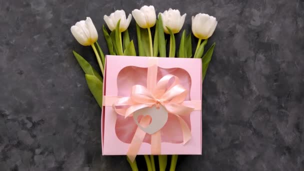白色郁金香花 带有粉色礼品盒和心脏卡标签 深色背景平铺 4K视频3月8日 快乐女性 母亲节的概念 — 图库视频影像