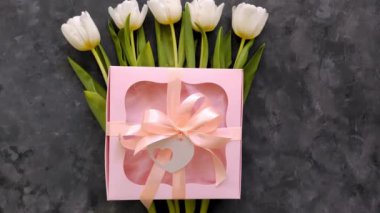 Beyaz lale çiçekleri, pembe hediye kutusu ve siyah arka planda kalp kartı etiketi, düz kaset 8 Mart Mutlu Kadınlar Anneler Günü konsepti. Çiçek buketi, kurdele yayı, kadın blog reklamı.