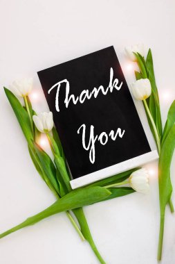 Siyah tahtada beyaz arka planda lale çiçekleri olan bir kart işareti var. Karatahta karşılama mesajı üst görünümü. Yeşil yapraklı doğal çiçek süslemesi. Şükran Günü pankartı