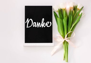 Beyaz arka planda lale çiçekleri olan siyah kartondaki Alman kartıyla teşekkür ederim. Karatahta mesaj iletisi üst görünümü. Doğal çiçekli yeşil yapraklar. Minnettar tırnak işareti.