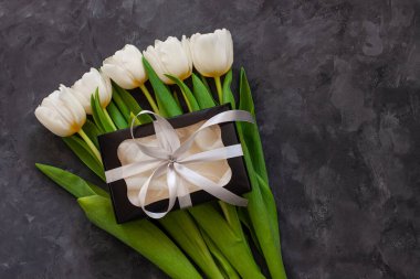 Beyaz lale çiçekleri ve siyah hediye kutusu. Metin 8 Mart Mutlu Kadınlar Anneler Günü için yer. Gümüş kurdeleli çiçek buketi, tebrik kartı. İnternet sitesi afişini üstten kopyala