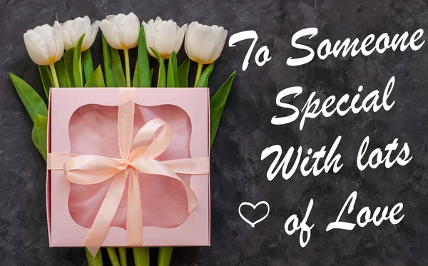 To Someone Special With Lots of Love card sign text. White tulip flowers and pink gift box with ribbon bow dark background flat lay. Flower bouquet greeting card. Copy space website banner top view.
