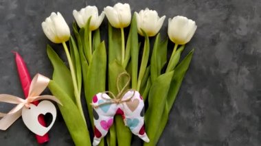 Beyaz lale çiçekleri buketi ve pembe kurdeleli kırmızı mum ve koyu arkaplanda kalpleri olan melek kanatları 4K 'lık üst manzara yatıyordu. Doğum günün kutlu olsun Paskalya 8 Mart Kadınlar Anneler Günü konsepti.