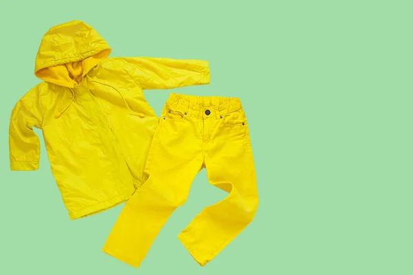 ネオミントの背景に黄色のレインコートとジーンズが隔離されています 明るいレインジャケット デニムパンツ 子供のスタイル外の服 雨と太陽をお楽しみください こんにちは秋 幸せな雨の日のコンセプトコピースペースフラットレイ — ストック写真