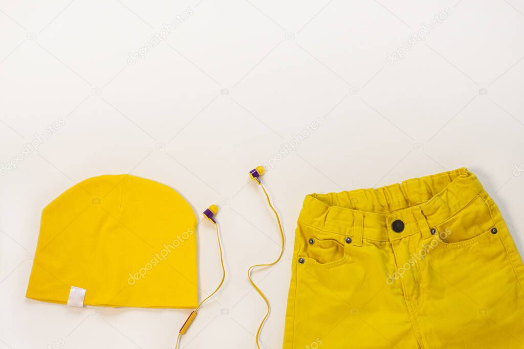 Yellow flat lay jeans, cotton hat and headphones on white background copy space,top view. Spring summer fashion, capsule wardrobe concept.Sport casual style,trendy bright colors clothing accessories