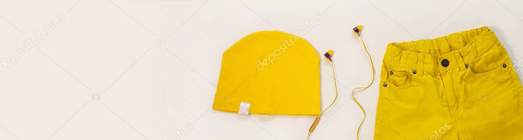 Yellow flat lay jeans, cotton hat and headphones on white background copy space site header.Spring summer fashion, capsule wardrobe concept.Sport casual style,trendy bright colors clothing accessories