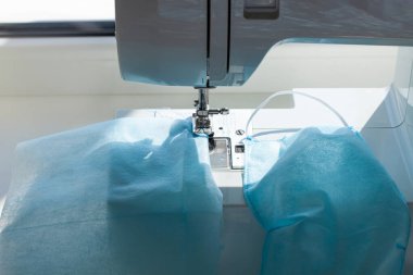 El yapımı Coronavirus hastalığına karşı yüz maskesi COVID-19 pandemisi. Bağcıklı dikiş makinesi, tıbbi malzeme sıkıntısı. Çözüm eksikliği, tozu, mikropları, ev yapımı virüs korumasını önler