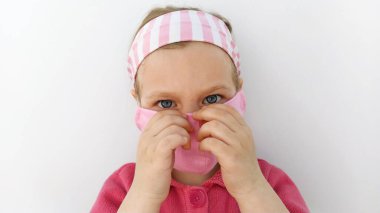 Koronavirüs COVID-19 salgınına karşı koruyucu pembe kumaş maskeli küçük bir kız. Wuhan virüs salgını. Karantina sırasında dikilmiş maskelerle çocukların el yapımı koruması.