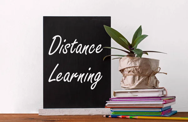 Chalboard Distance learning, books stack, pencils with green home plant in a pot wrapped in brown kraft paper on white background. Online education, quarantine e-learning mockup, back to school banner