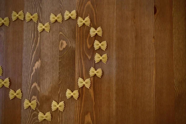 Pasta mariposas o arcos, farfalle dispuestos en forma de un pedazo de corazón en un árbol . — Foto de Stock