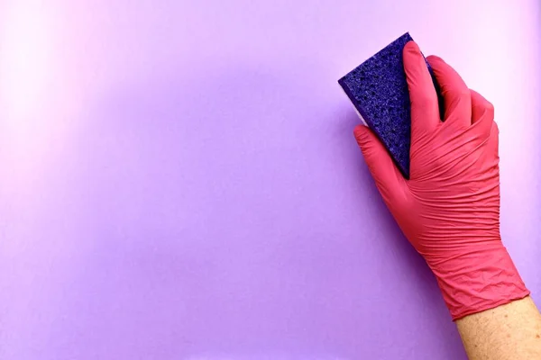 Prawa ręka w gumowej rękawiczce z gąbką celulozową, porowatą powierzchnią, na fioletowym tle. — Zdjęcie stockowe