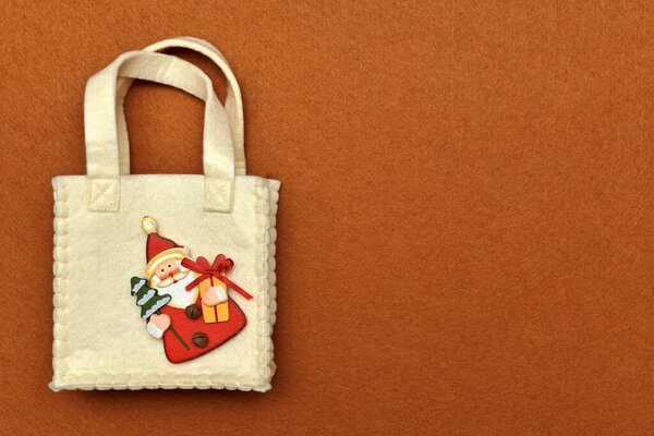  Handbag with handles, with decorative wooden figurine of Santa Claus sewn in the corner, on a red felt background.