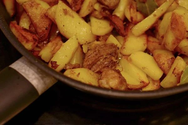 Aardappelen gebakken met vlees in een glanzende koekenpan tegen een donkere achtergrond. — Stockfoto