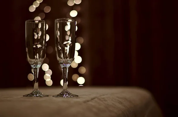 Dois copos de vinho na colcha do lado esquerdo contra o pano de fundo de cortinas escuras com uma grinalda brilhante de luzes . — Fotografia de Stock
