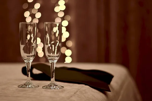 Duas taças de vidro na beira da cama no quarto, ao lado de um homem amarrado entre as luzes imitando bolhas de champanhe . — Fotografia de Stock