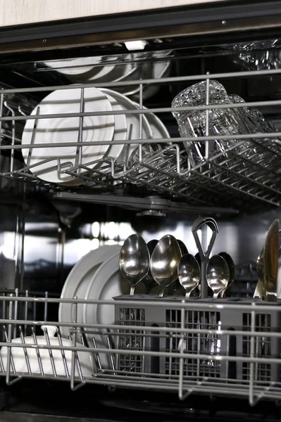 A fragment of the inside of the dishwasher with clean dishes shot in perspective in a vertical style.