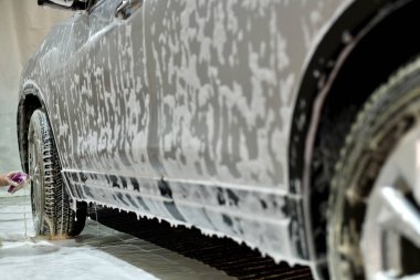  O, çalışan bir deterjan yardımıyla ön tekerlekleri temizledi ve arabayı sabunlu köpükle doldurdu..