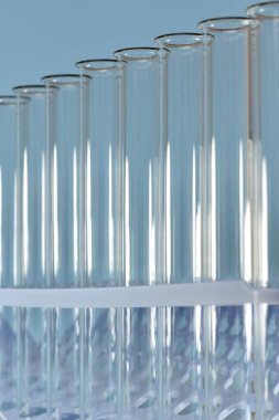 Mavi arka plandaki tepside bulunan şeffaf test tüplerinin dikey görüntüsü.