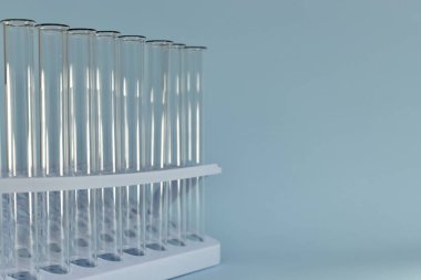 Sol taraftaki mavi bir arkaplanda, şeffaf test tüplerinin yatay görüntüsü..